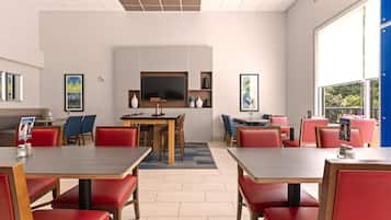 A modern dining area with red upholstered booths and wooden tables, a flat-screen TV mounted above a wooden counter, and large windows offering a view of greenery.