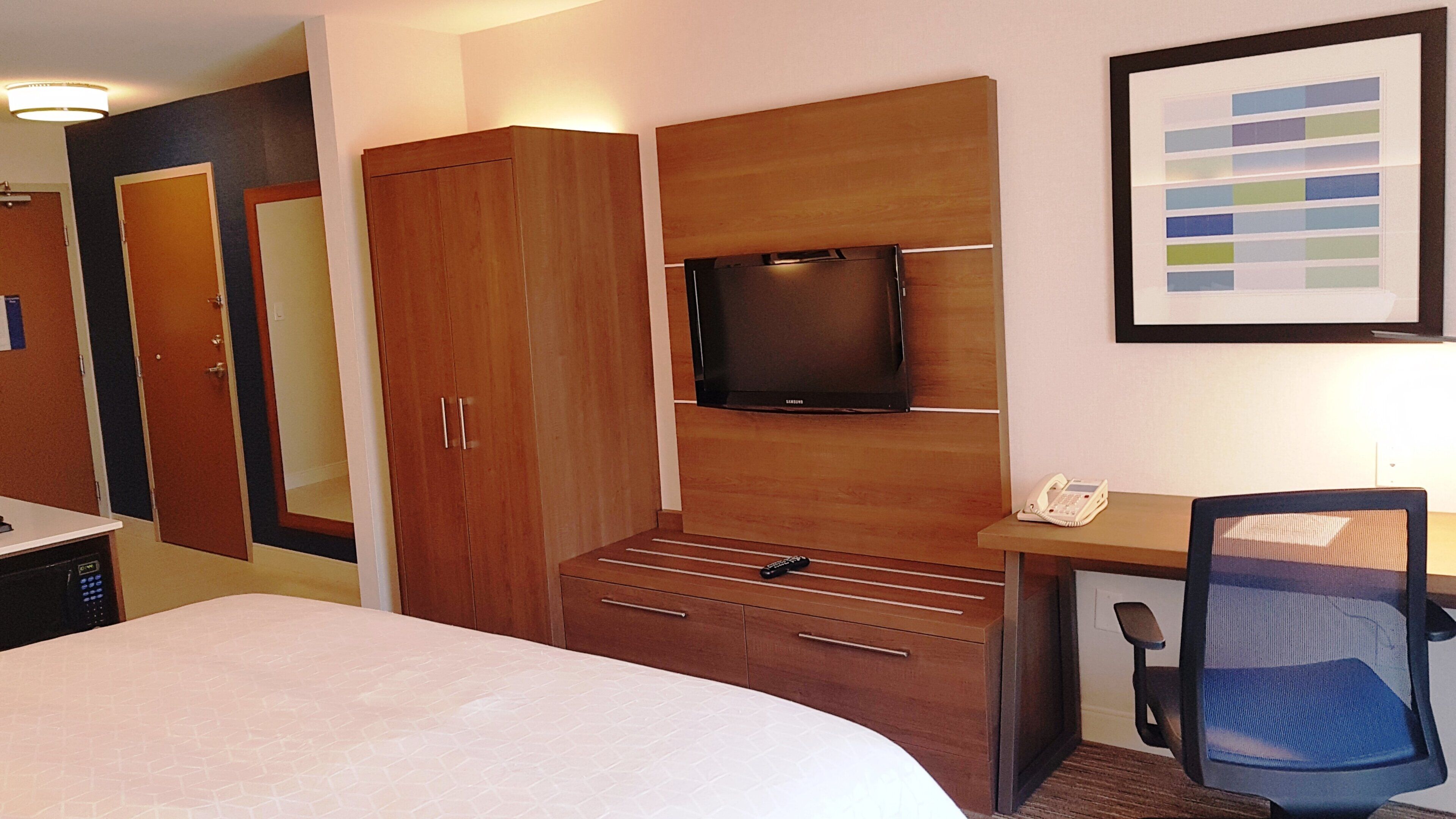 Habitación de hotel con una cama, un escritorio con teléfono, televisión y armario.