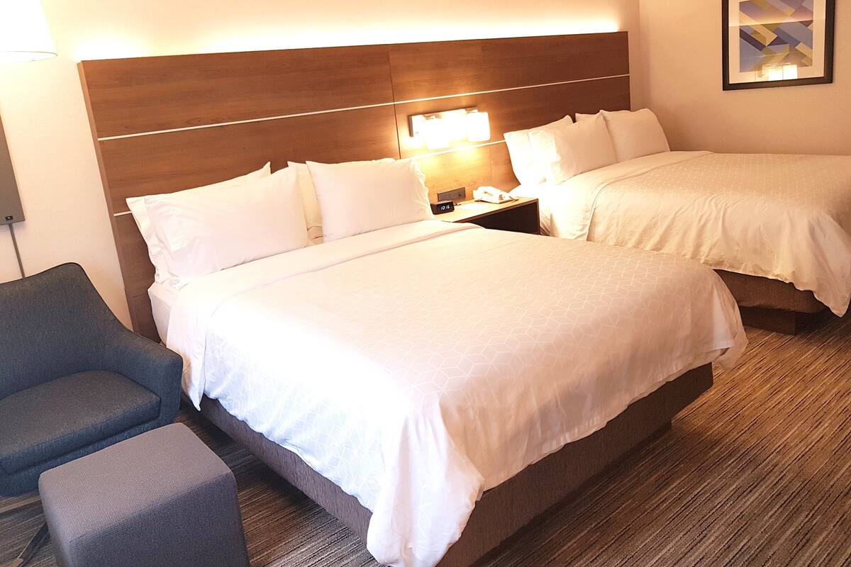 A hotel room with two beds, a nightstand, a lamp, a chair, and a framed picture on the wall.