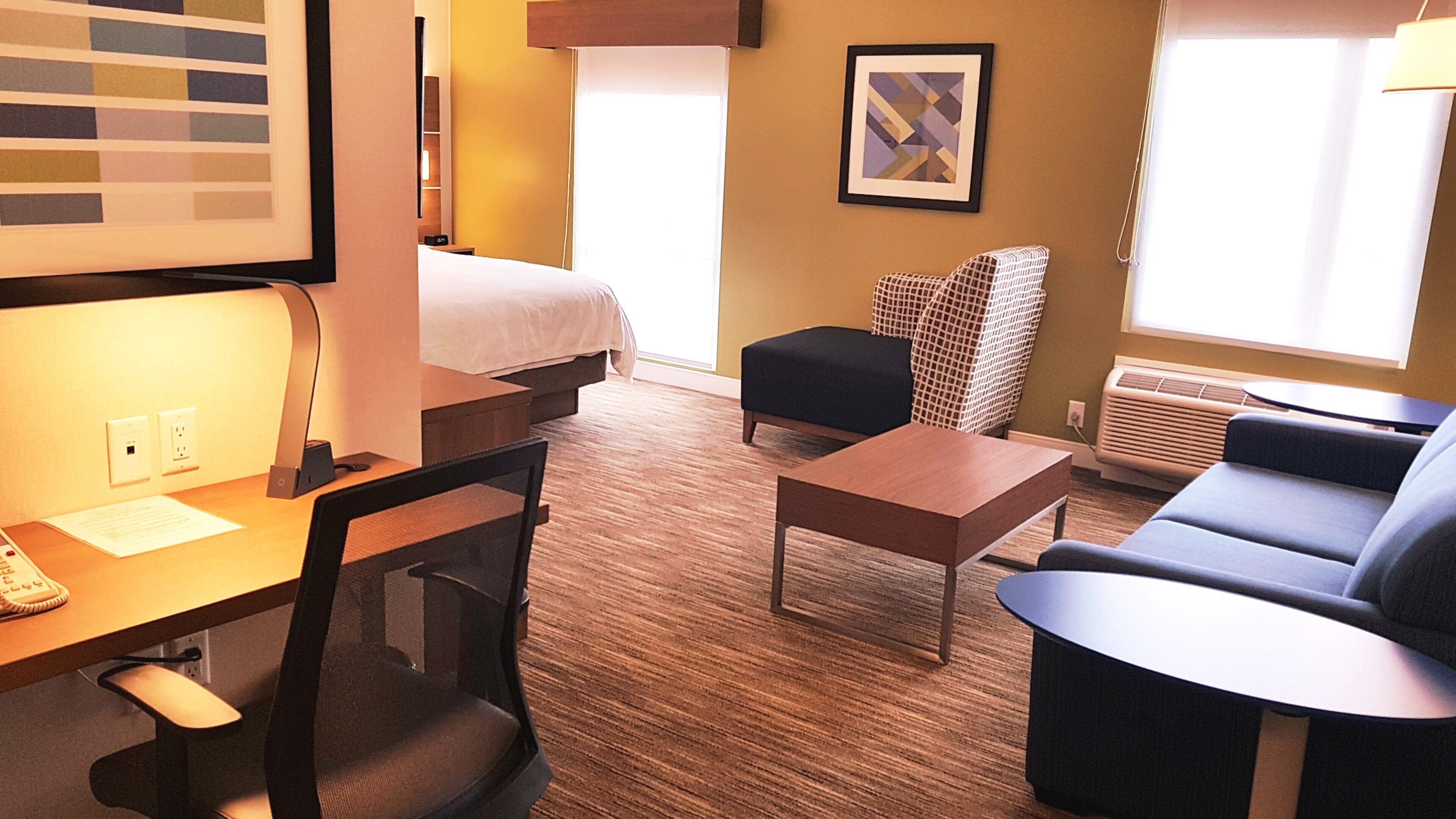 A hotel room with a bed, desk, chair, sofa, and a framed picture on the wall.