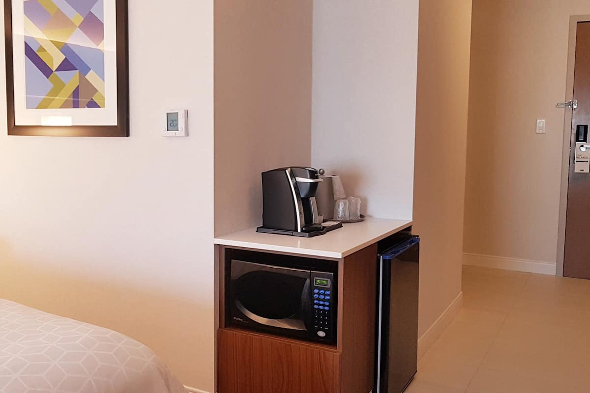 A hotel room with a bed, a microwave, a coffee maker, and a framed abstract artwork on the wall.