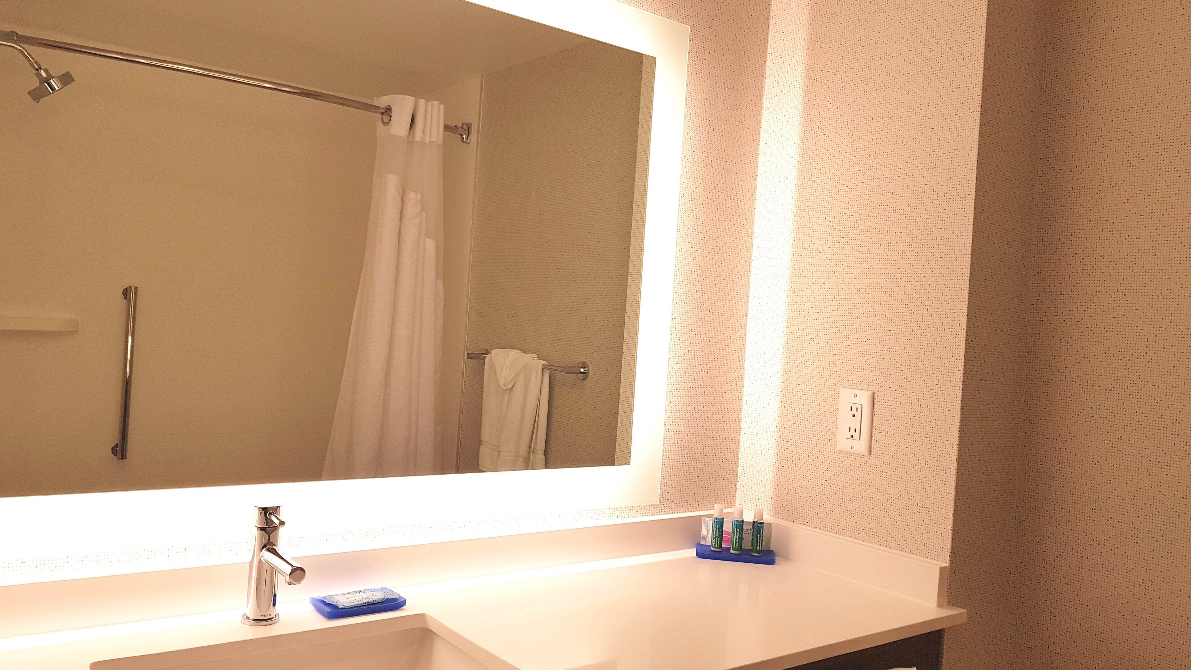 Une salle de bain avec un grand miroir, un lavabo, une douche et un porte-serviettes.