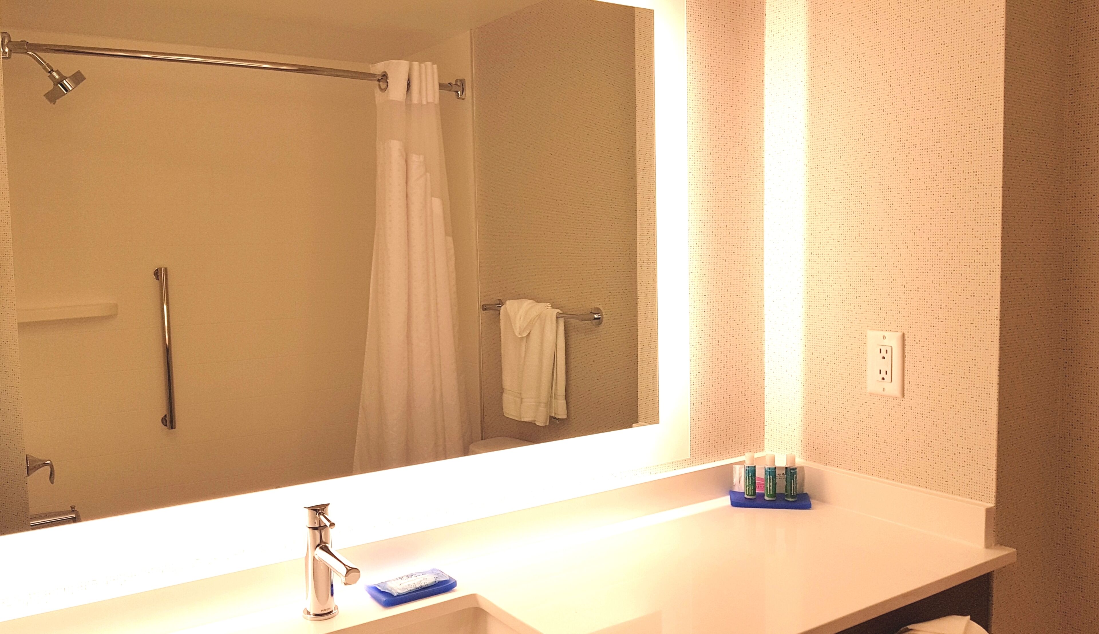 A bathroom with a large mirror, a sink, a shower, and a towel rack.
