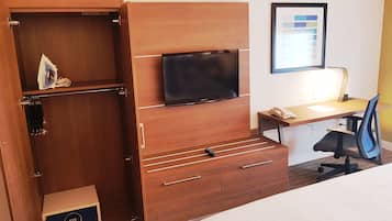Habitación de hotel con cama, escritorio con silla, televisor, armario y un cuadro en la pared.