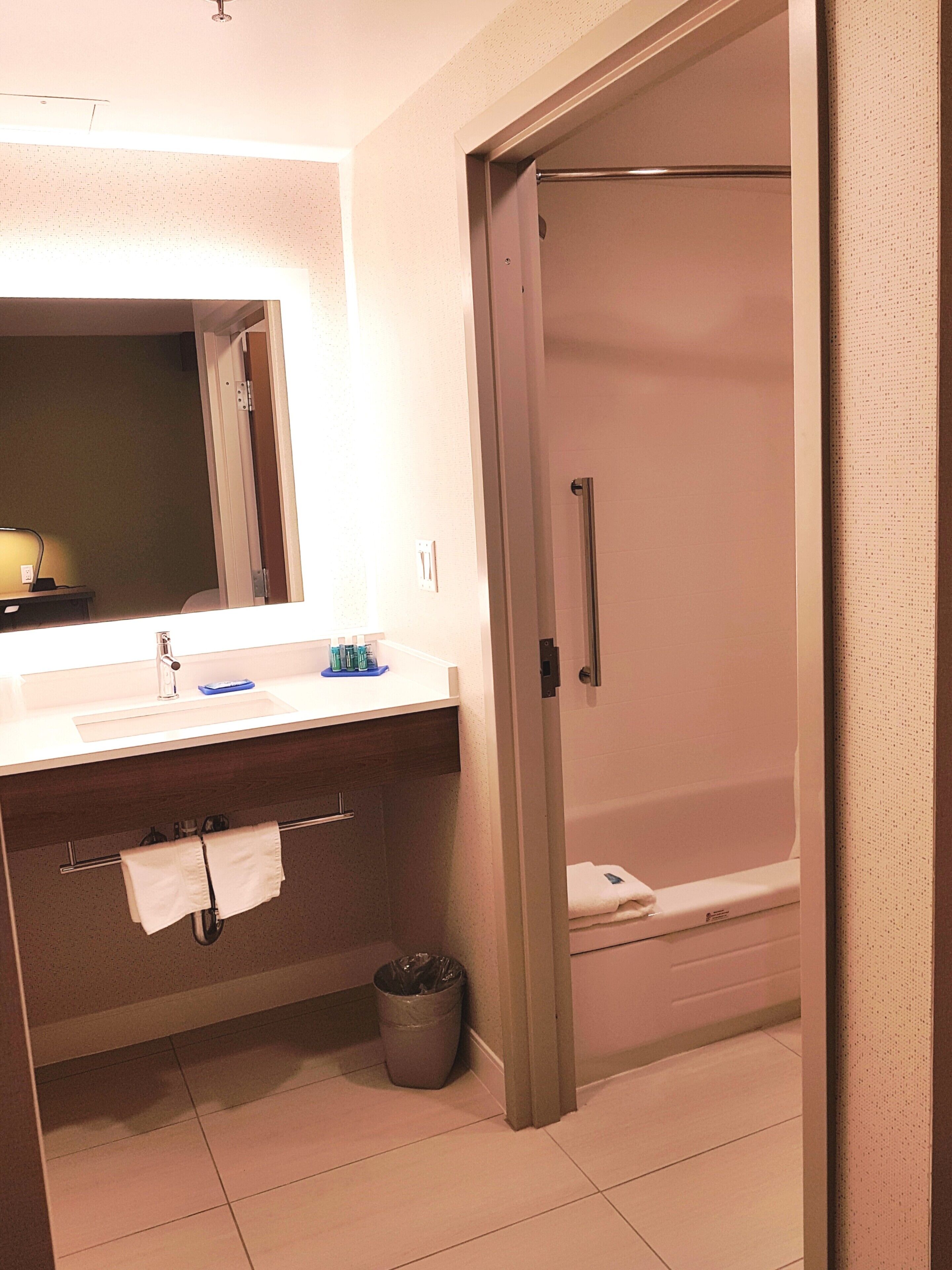 A bathroom with a sink, mirror, towel rack, and a shower area.