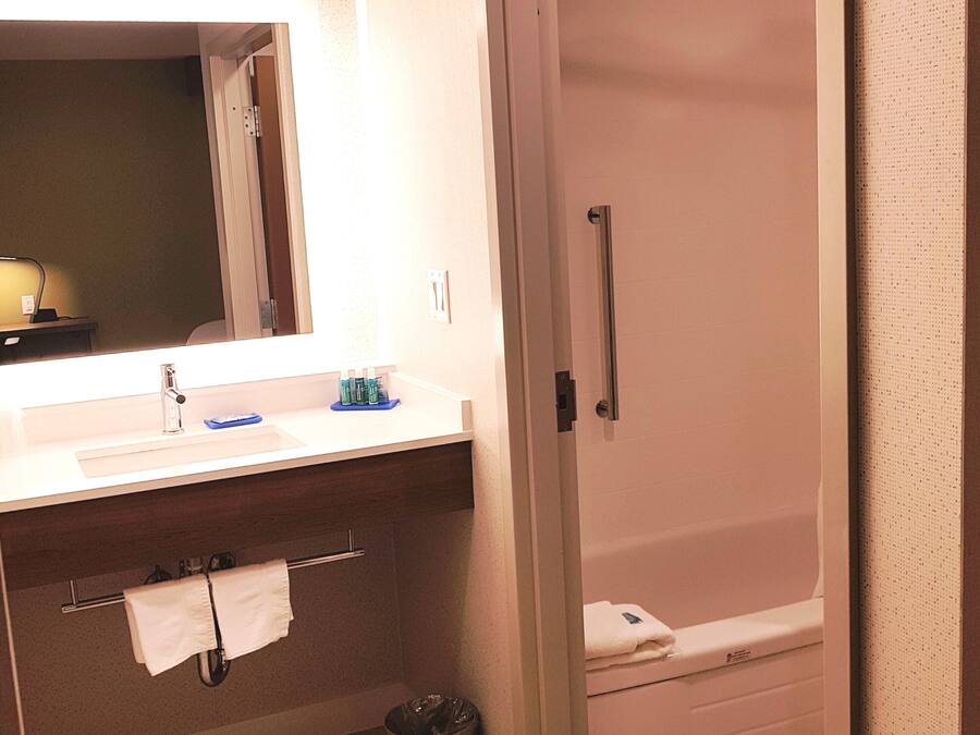 A bathroom with a sink, mirror, towel rack, and a shower area.