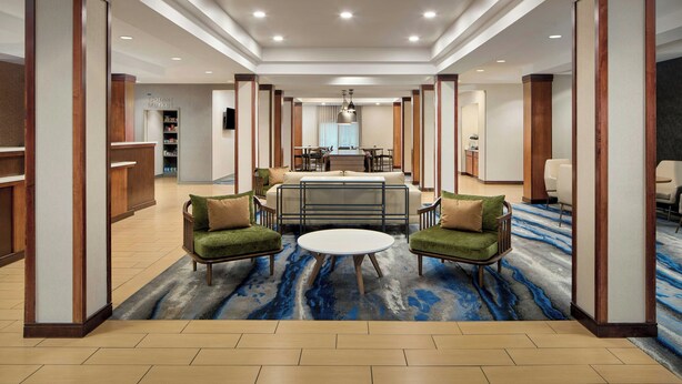 A hotel lobby with a reception desk, a dining area, and seating with a blue patterned carpet. - Fairfield Inn & Suites by Marriott Frankfort (Frankfort)