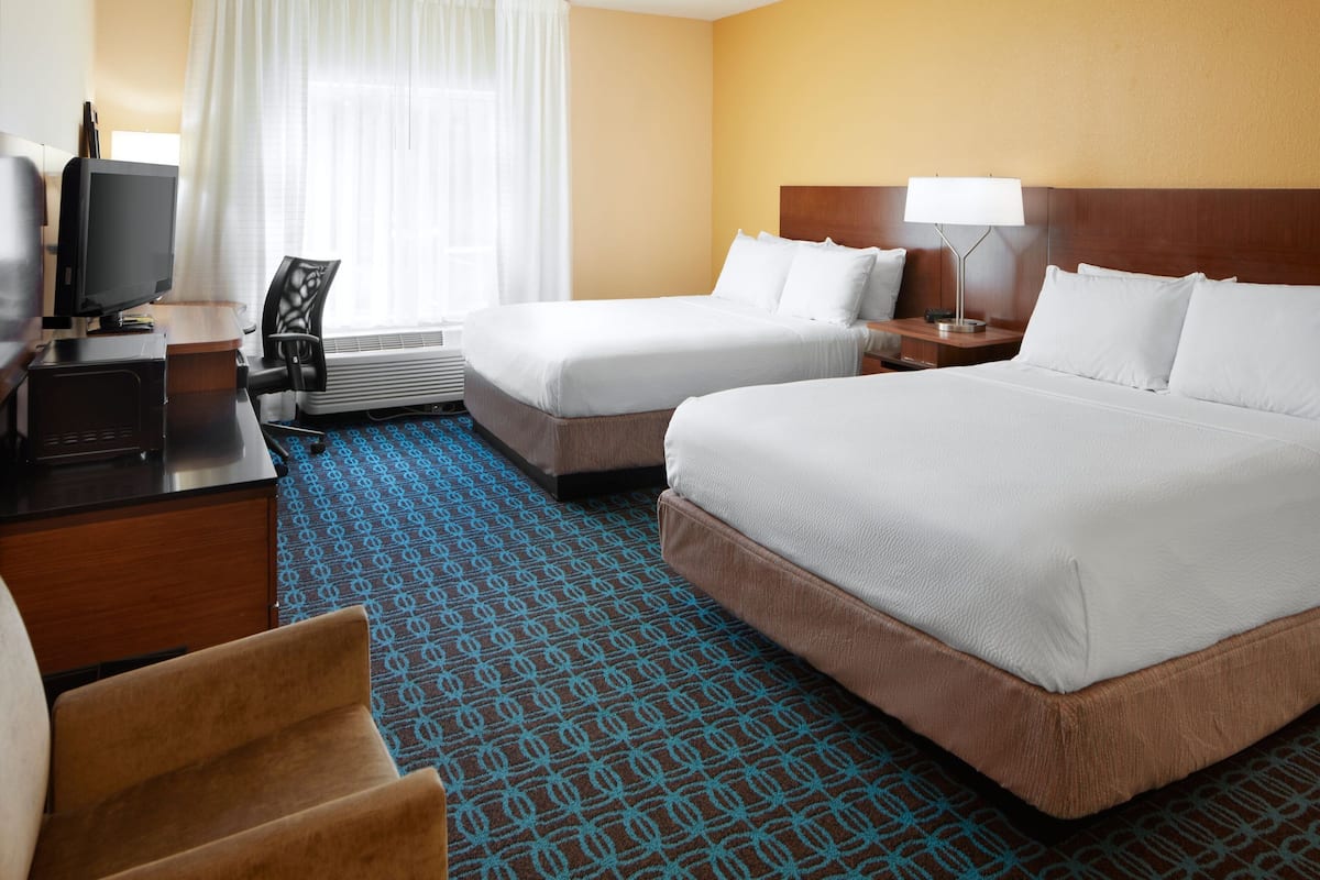 A hotel room with two beds, a desk with a computer, a chair, and a TV.