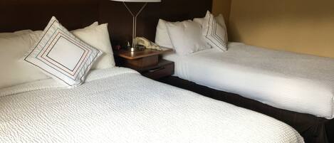 Habitación de hotel con dos camas, una mesita de noche con lámpara, un reloj y un teléfono.