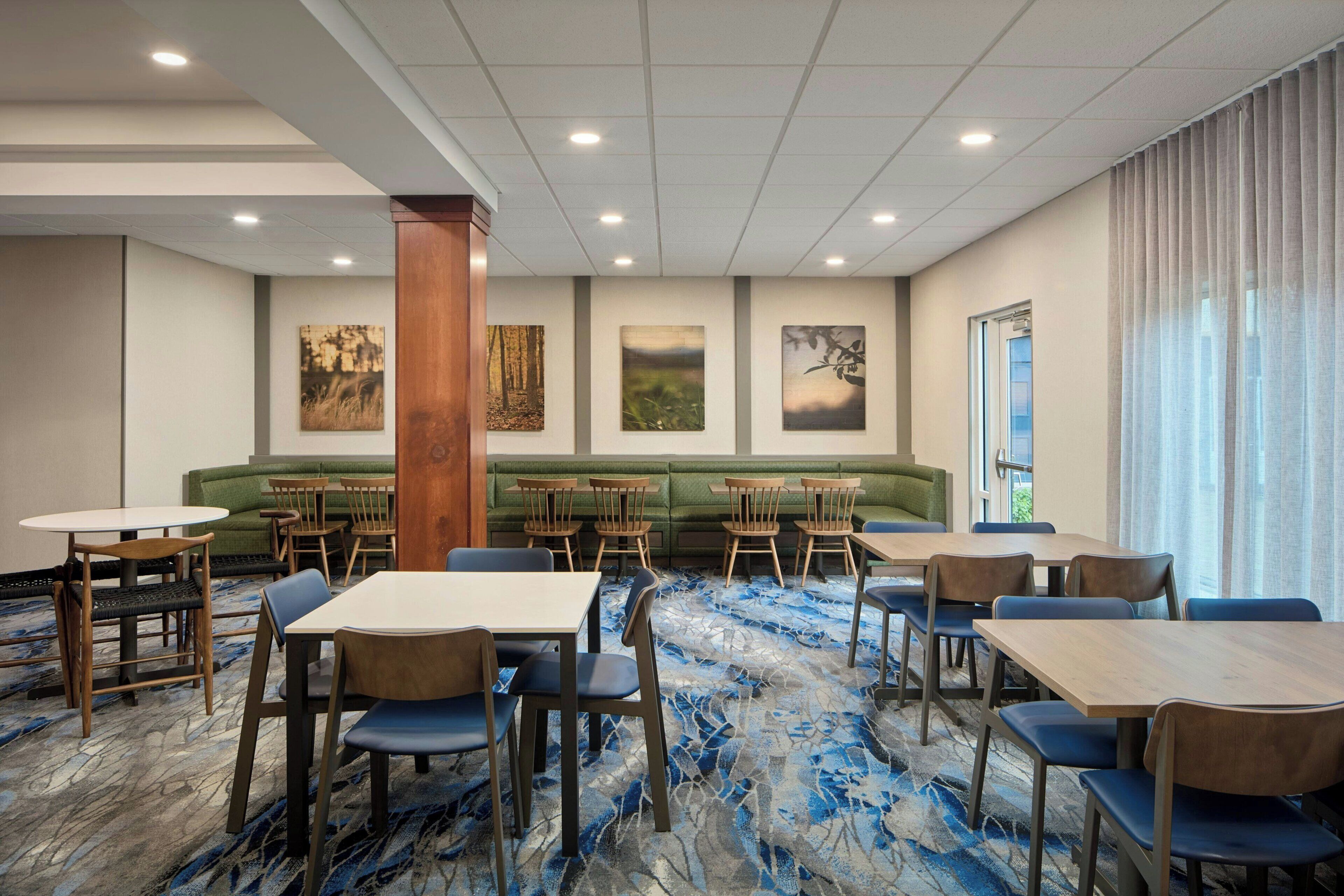 Une salle à manger d’hôtel avec des tables, des chaises, un canapé vert et des œuvres d’art accrochées aux murs.