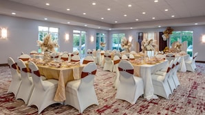 Un salón de banquetes con mesas redondas, sillas blancas con cintas marrones y centros de mesa florales.