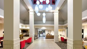 Eine geräumige Hotelhalle mit einer zentralen Rezeption, roten Sesseln und einer modernen Kronleuchter.
