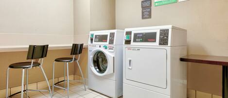 A laundry area with two washers and dryers, a chair, and a wall-mounted instruction poster.
