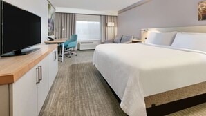 Ein Hotelzimmer mit einem großen Bett, einem Schreibtisch mit Computer, einem Fernseher und einem Sessel.