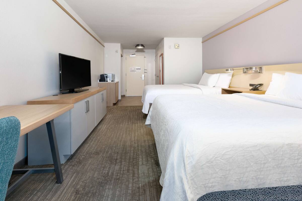 A hotel room with a desk, TV, two beds, and a bathroom door.
