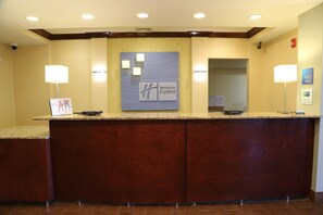 A reception desk with a wooden finish, a Holiday Inn Express logo, and two wall-mounted lamps. - Holiday Inn Express Hotel & Suites Cleveland by IHG (Cleveland)