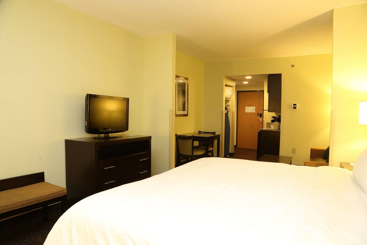 A hotel room with a large bed, a television on a dresser, a desk, and a chair.