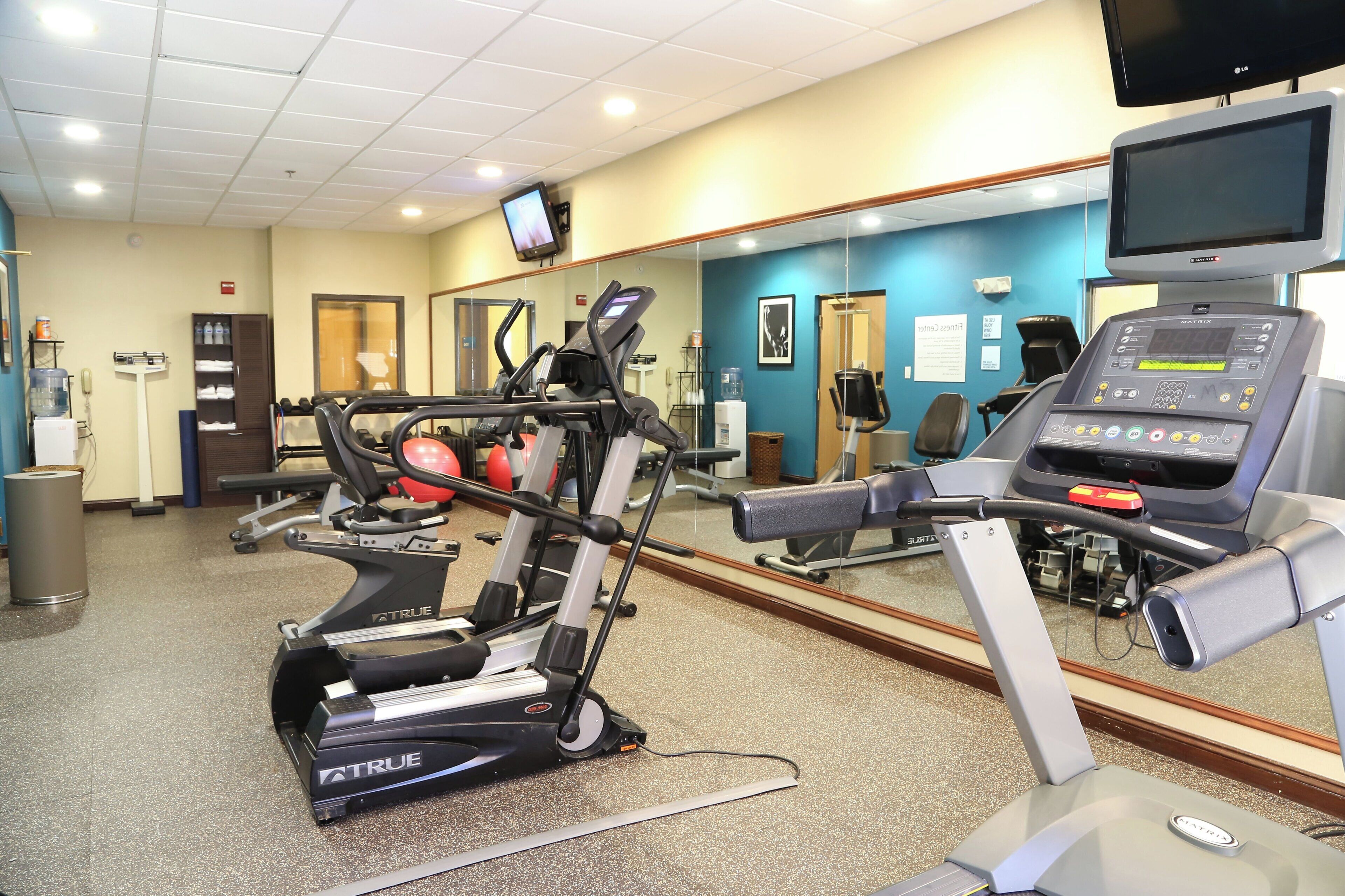 A gym with various exercise equipment, including treadmills and a stationary bike, and a large mirror reflecting the space.