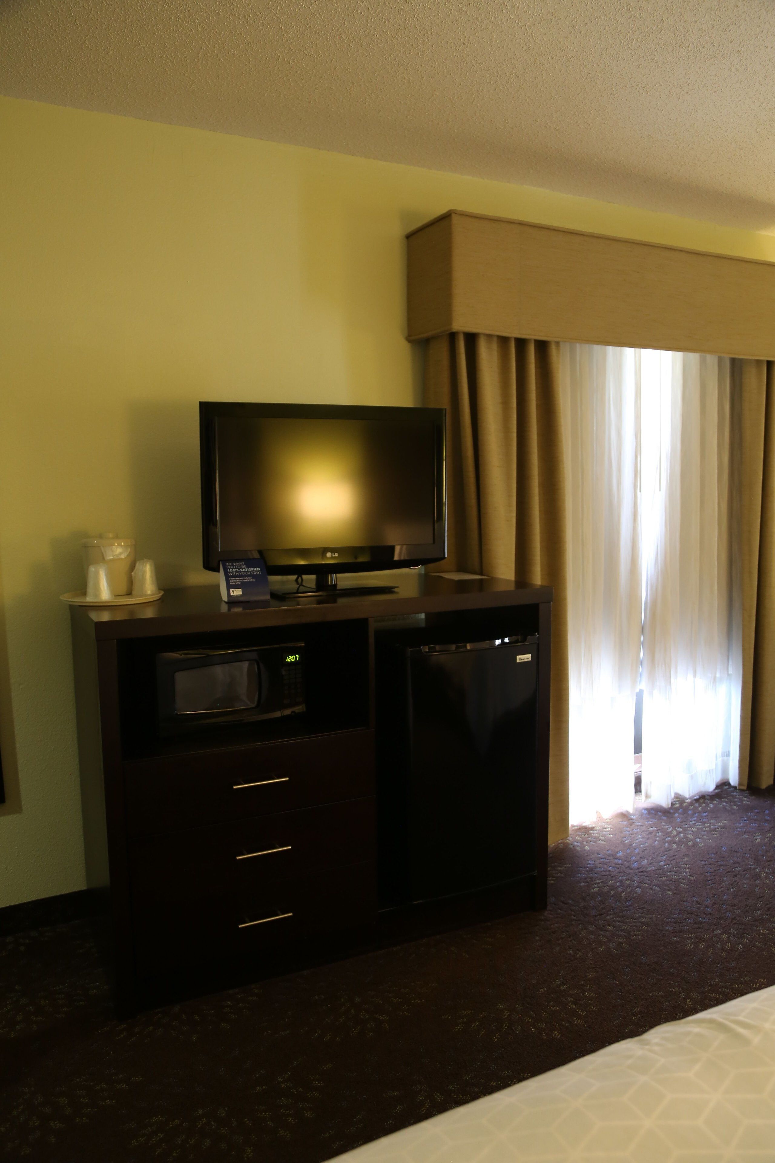 A hotel room with a flat-screen TV, a minibar, and a bed.