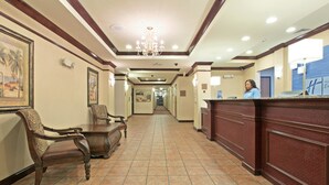 Um saguão de hotel com balcão de recepção, cadeiras e um corredor que leva à saída.