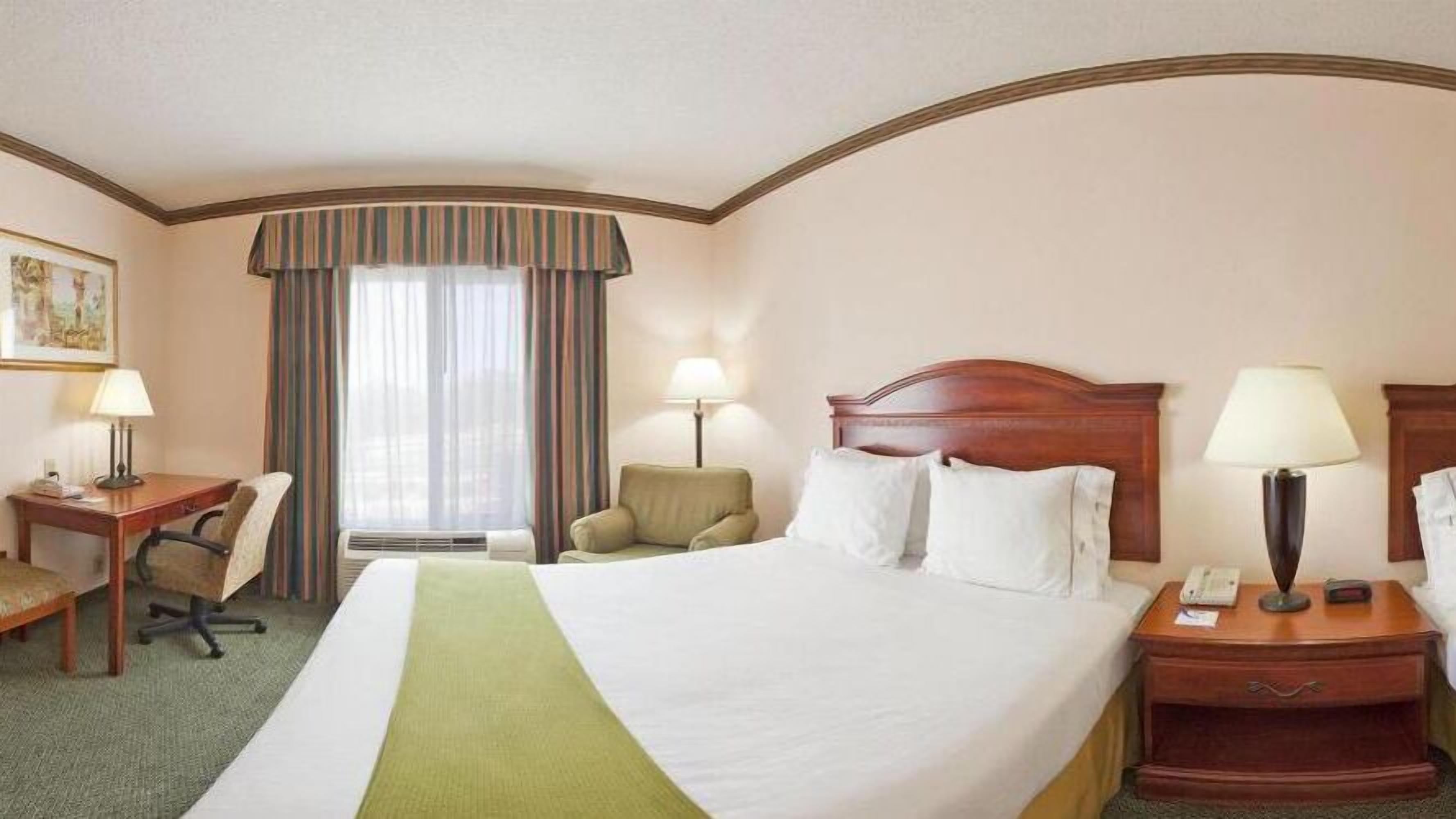 Une chambre d’hôtel avec un grand lit, un bureau, une chaise, une table de chevet et une lampe.