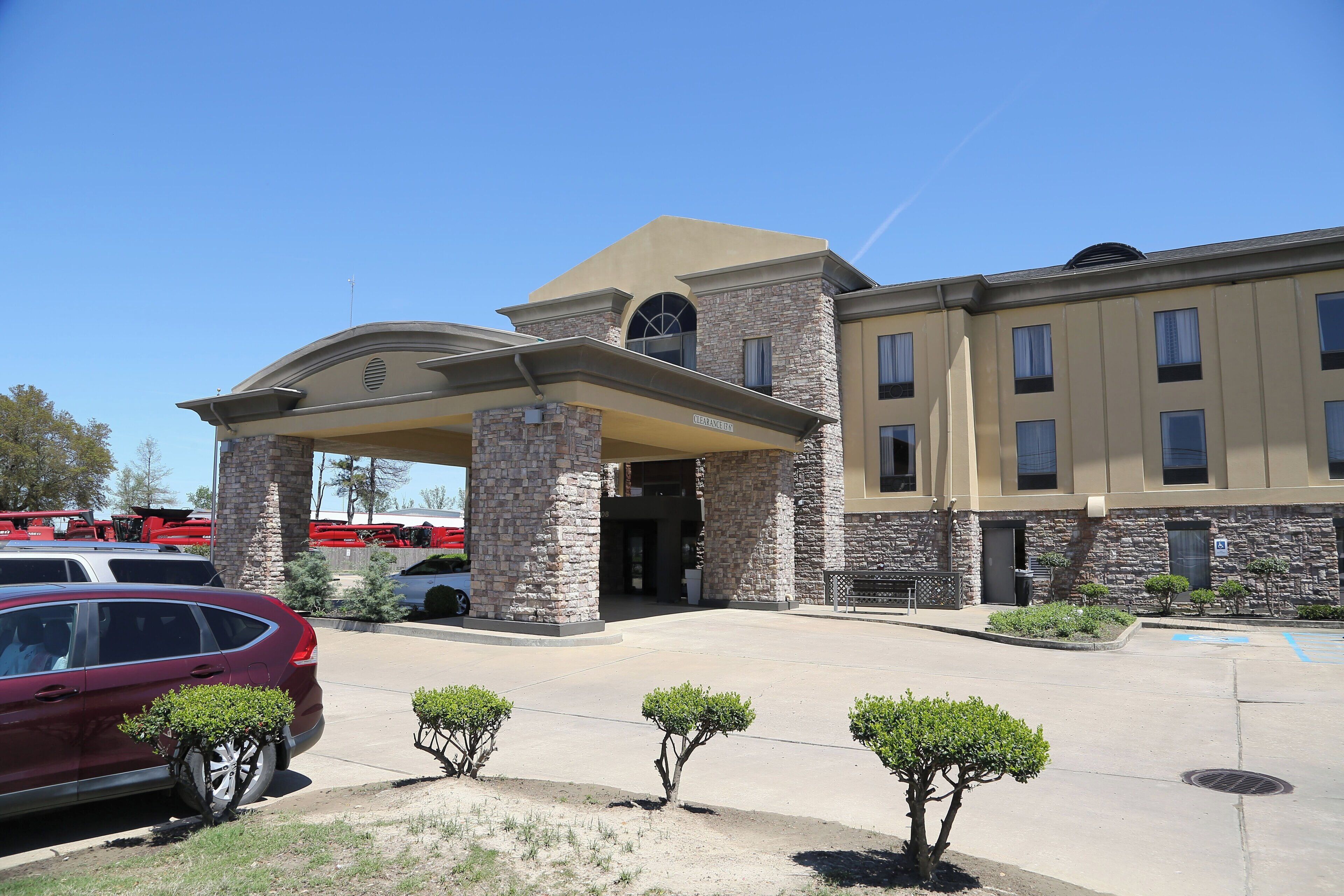 A building with a stone facade, a covered entrance, and a parking lot with a red car.