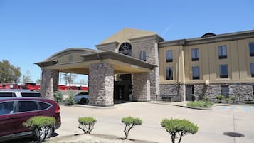 A building with a stone facade, a covered entrance, and a parking lot with a red car.
