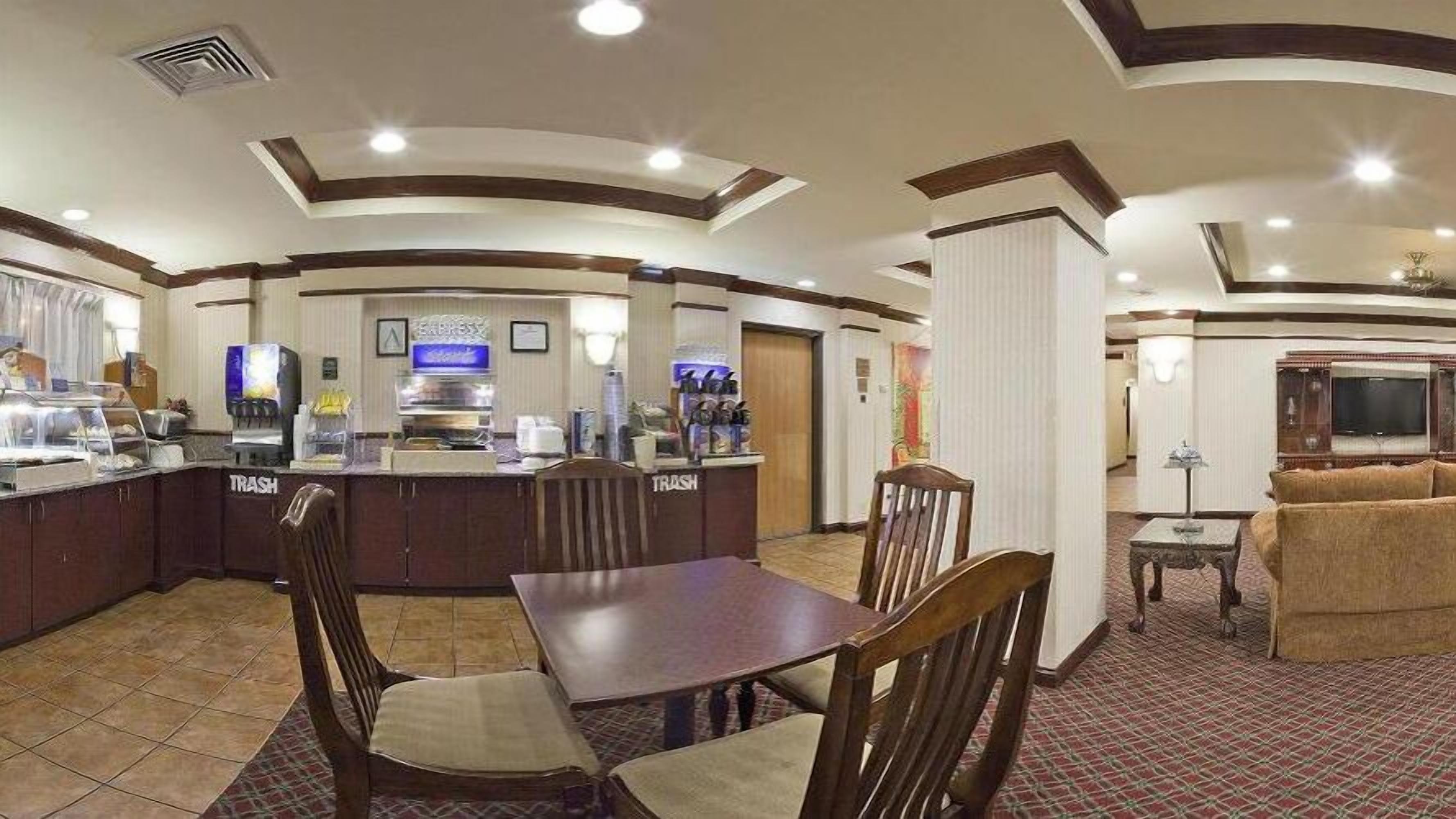 A hotel lobby with a central bar area, a dining table with chairs, and a seating area with a sofa.