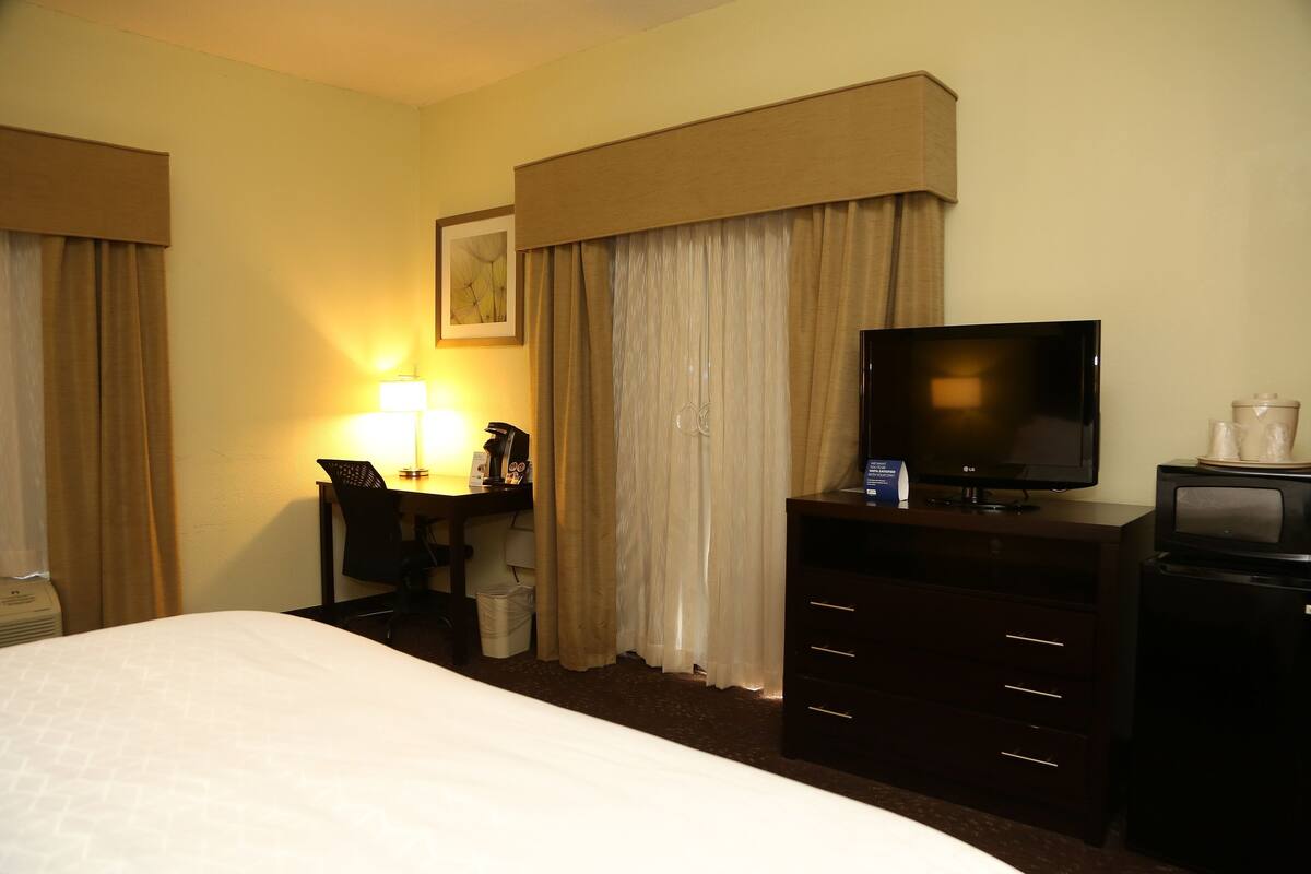A hotel room with a bed, a desk with a lamp, a television, and a minibar.