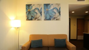 Um saguão de hotel com um sofá de couro marrom, duas almofadas listradas, um abajur e duas pinturas florais na parede.