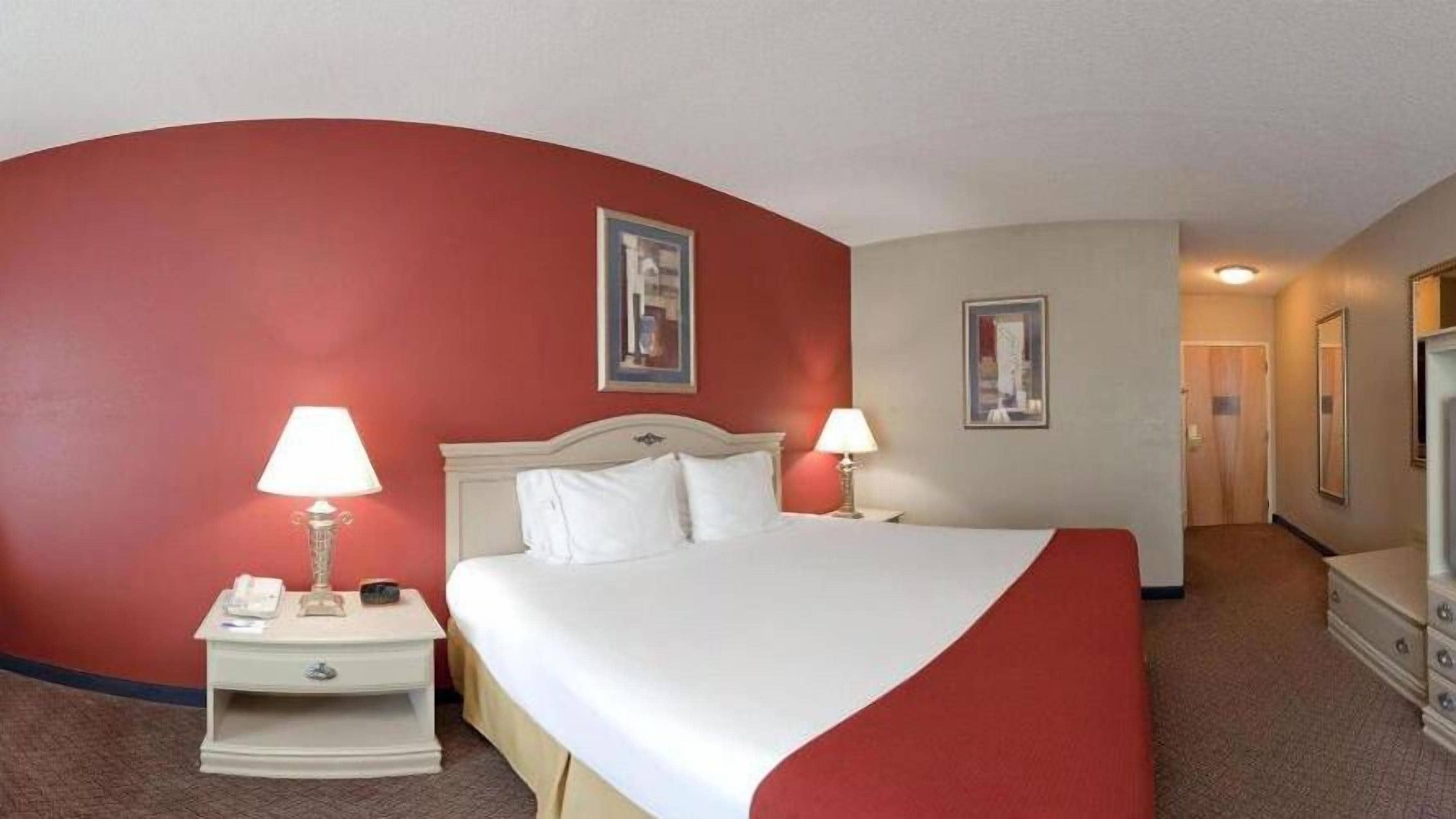 A hotel room with a large bed, two bedside tables with lamps, a dresser, and two framed pictures on the walls.