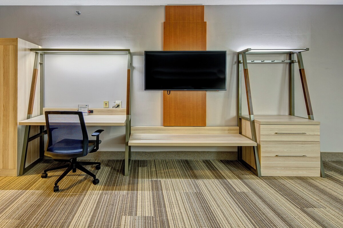 A room with a desk, chair, wardrobe, and a TV mounted on the wall.
