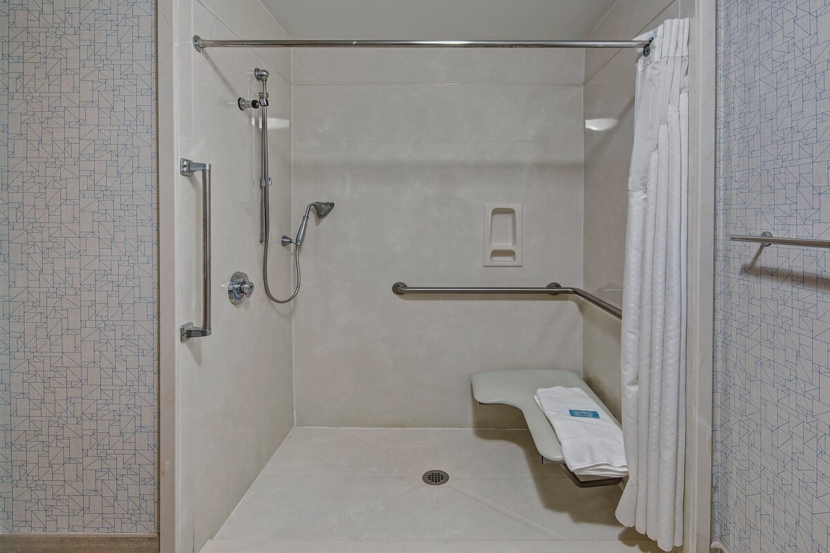 A walk-in shower with a grab bar, a white towel, and a showerhead.