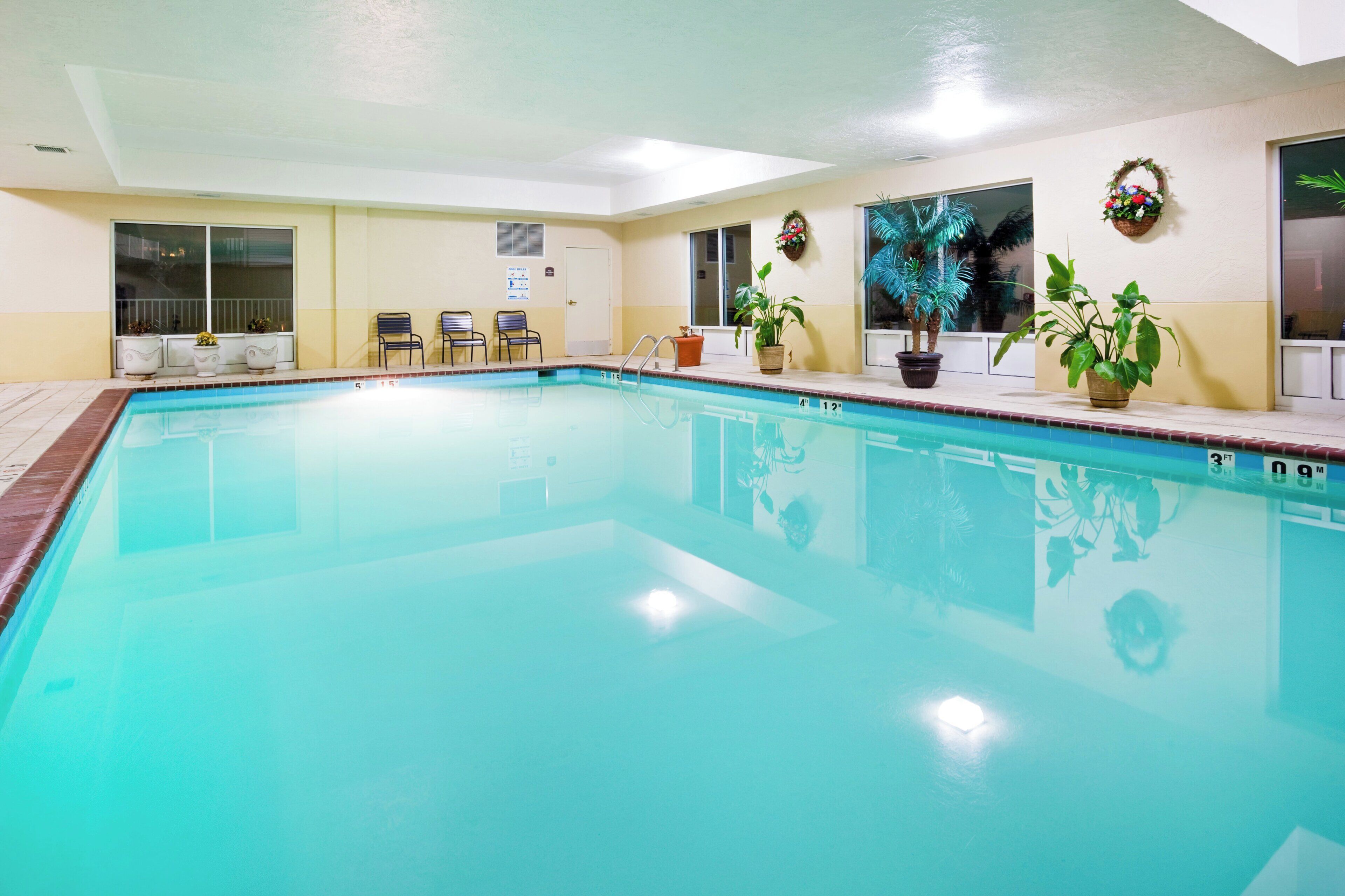 A large indoor swimming pool with clear water, surrounded by lounge chairs and potted plants.