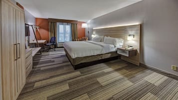 A hotel room with a bed, bedside table, lamp, desk, chair, and wardrobe.