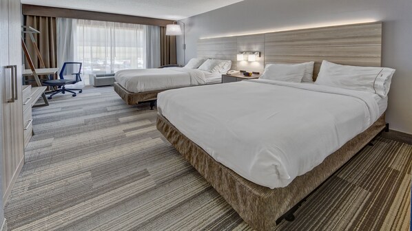 A hotel room with two beds, a desk, a chair, and a large window with curtains.