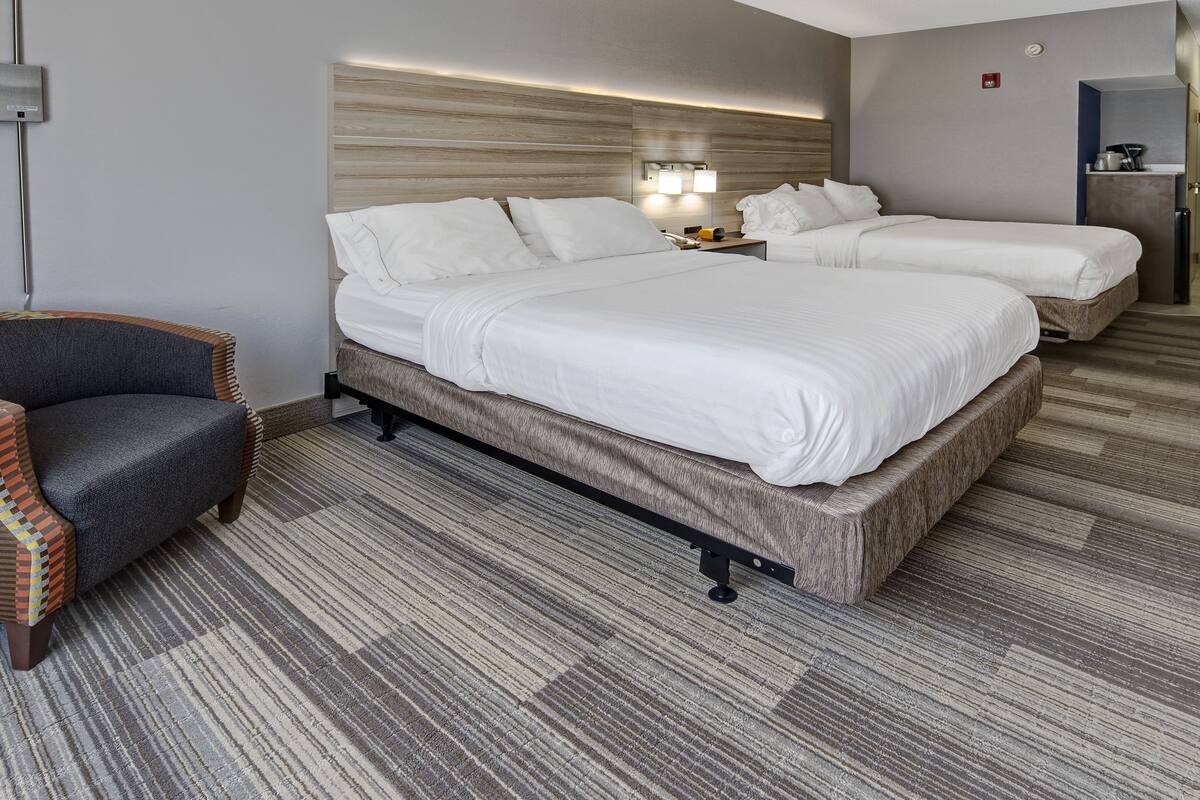 A hotel room with a large bed, a smaller bed, a chair, and a desk with a lamp.