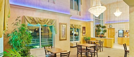Un hall de hotel con suelo a cuadros, mesas y sillas de madera, una zona de bar y grandes ventanales.