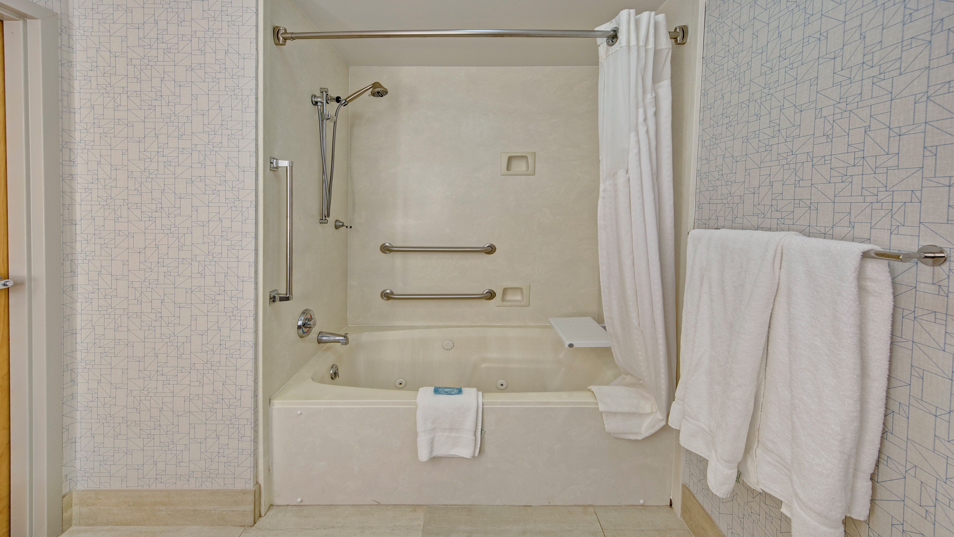 Ein Badezimmer mit Badewanne, Dusche, Handläufen und einem Handtuchhalter.