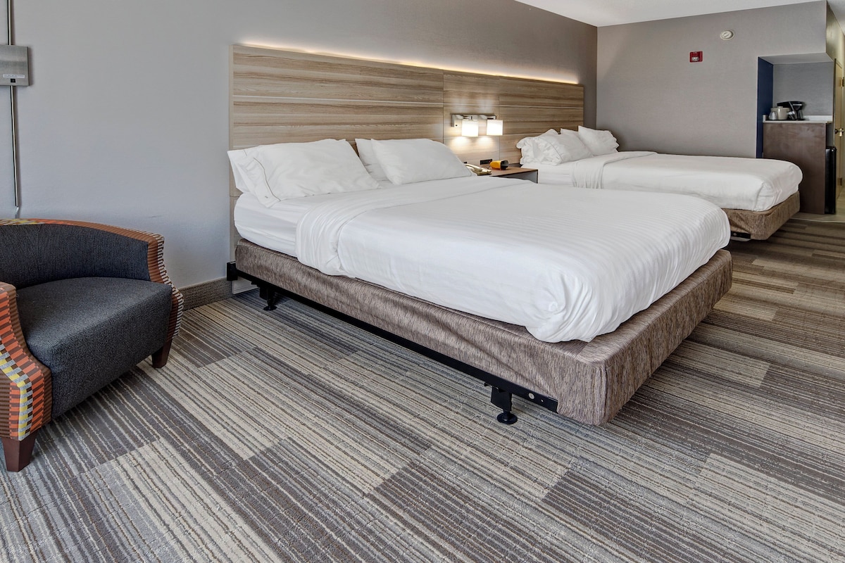 A hotel room with a large bed, a smaller bed, a chair, and a desk with a lamp.