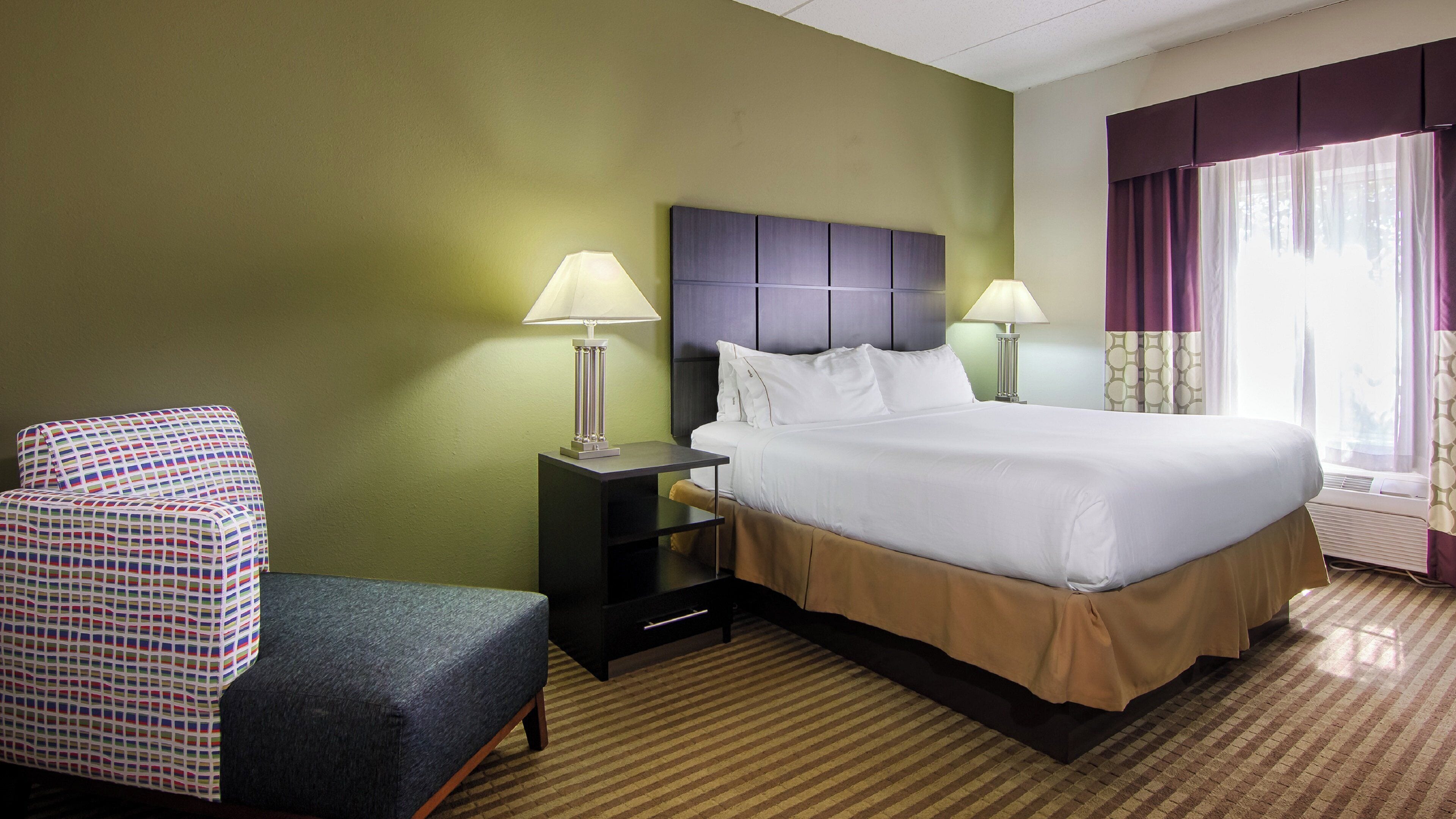 A hotel room with a bed, two bedside tables with lamps, a chair, and a window with curtains.