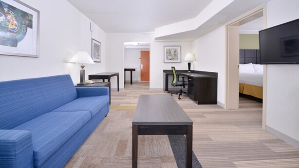 A hotel room with a blue sofa, a desk with a chair, a television, and artwork on the walls. - Holiday Inn Express Hotel & Suites Mooresville - Lake Norman by IHG (Mooresville)