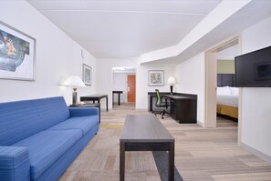 Habitación de hotel con un sofá azul, un escritorio con una silla, un televisor y obras de arte en las paredes.