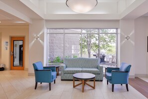 Un hall con sofá, dos sillones, una mesa de centro y un ventanal con vistas a árboles y edificios.
