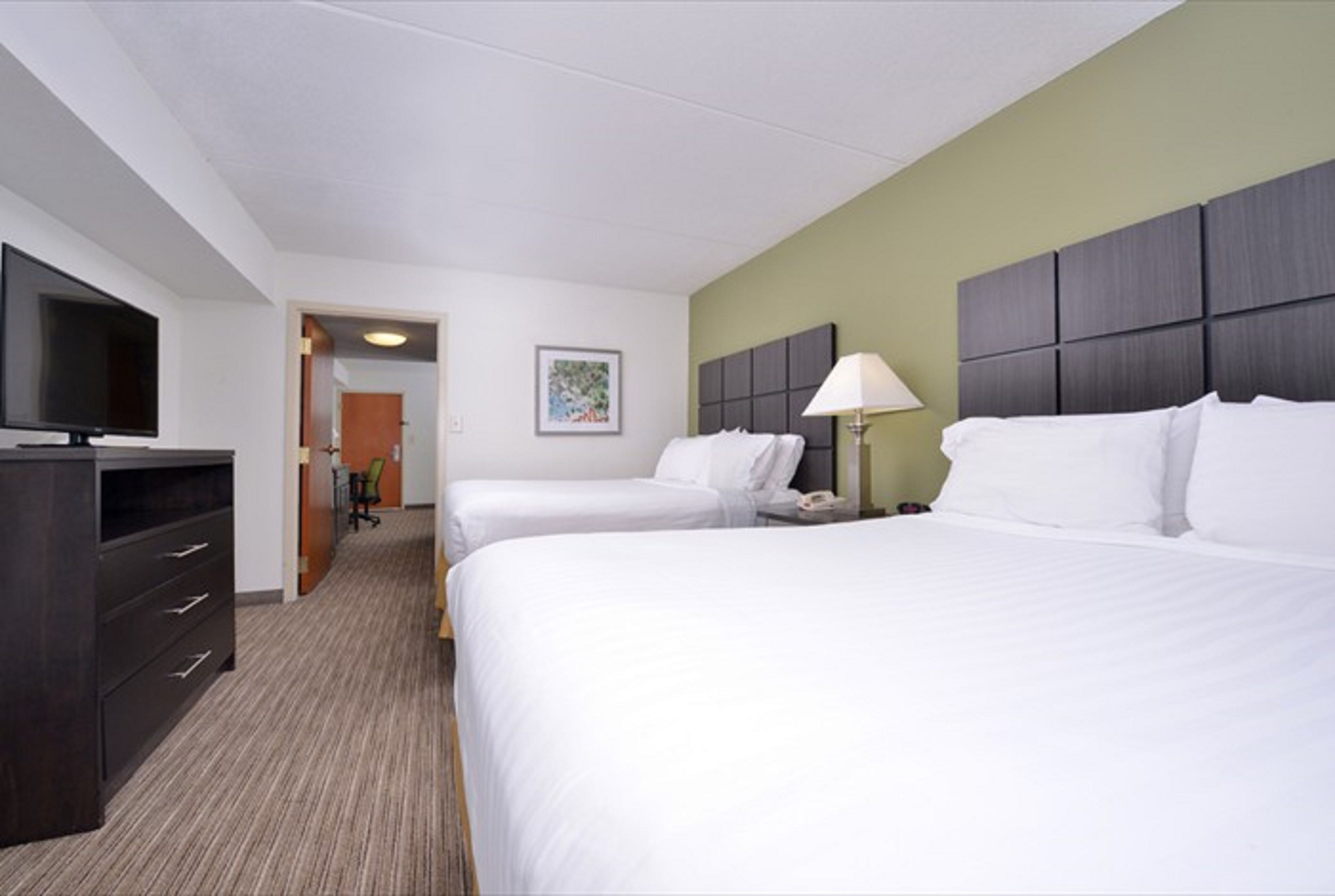 A hotel room with two beds, a TV, a desk, and a lamp.