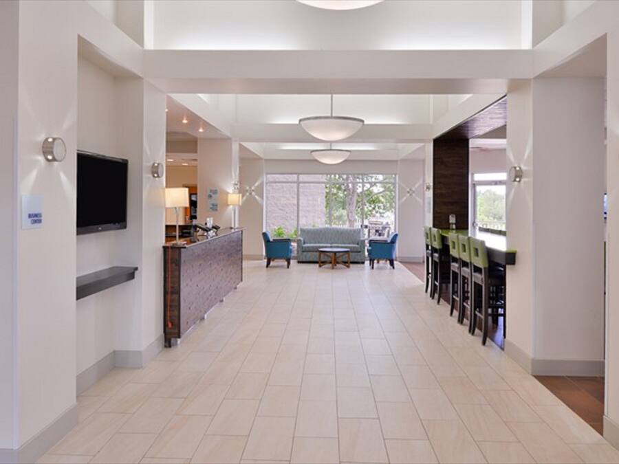 A spacious hotel lobby with a flat-screen TV, a reception desk, a seating area with sofas and chairs, and a dining area with tables and chairs.