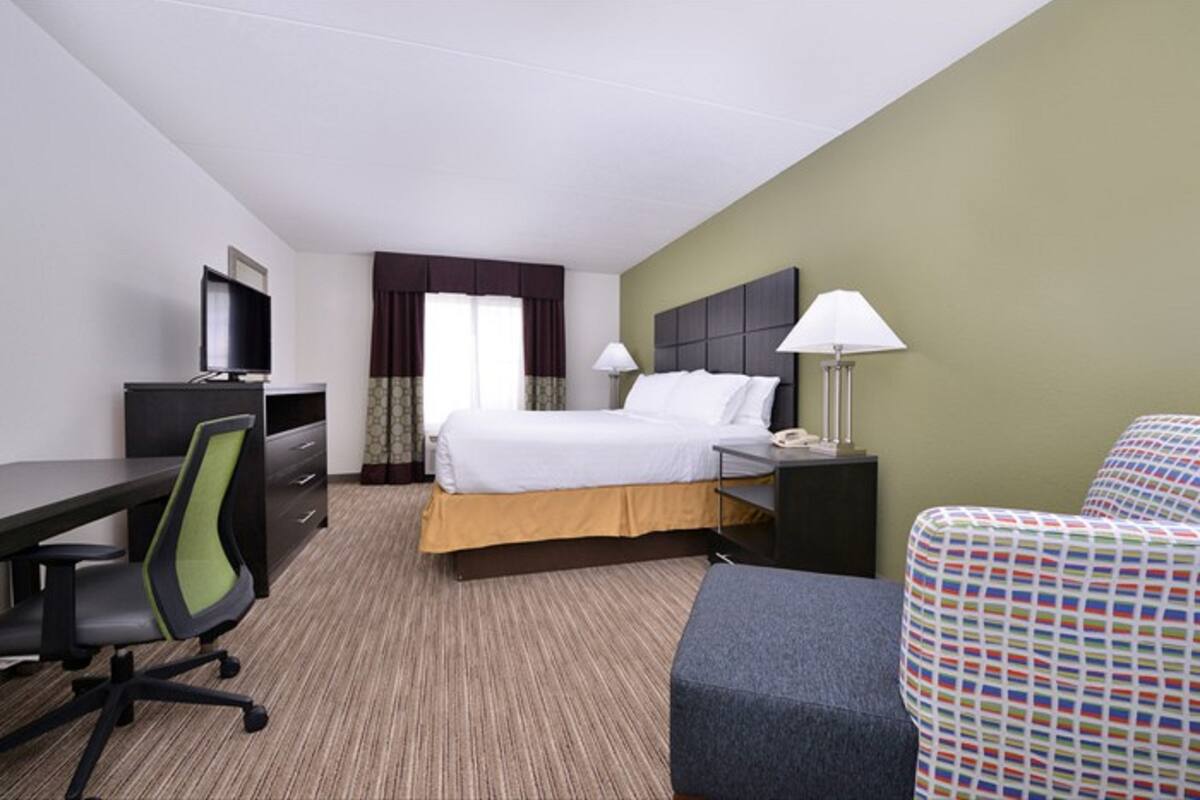 Habitación de hotel con cama, escritorio, silla, lámpara y televisor.