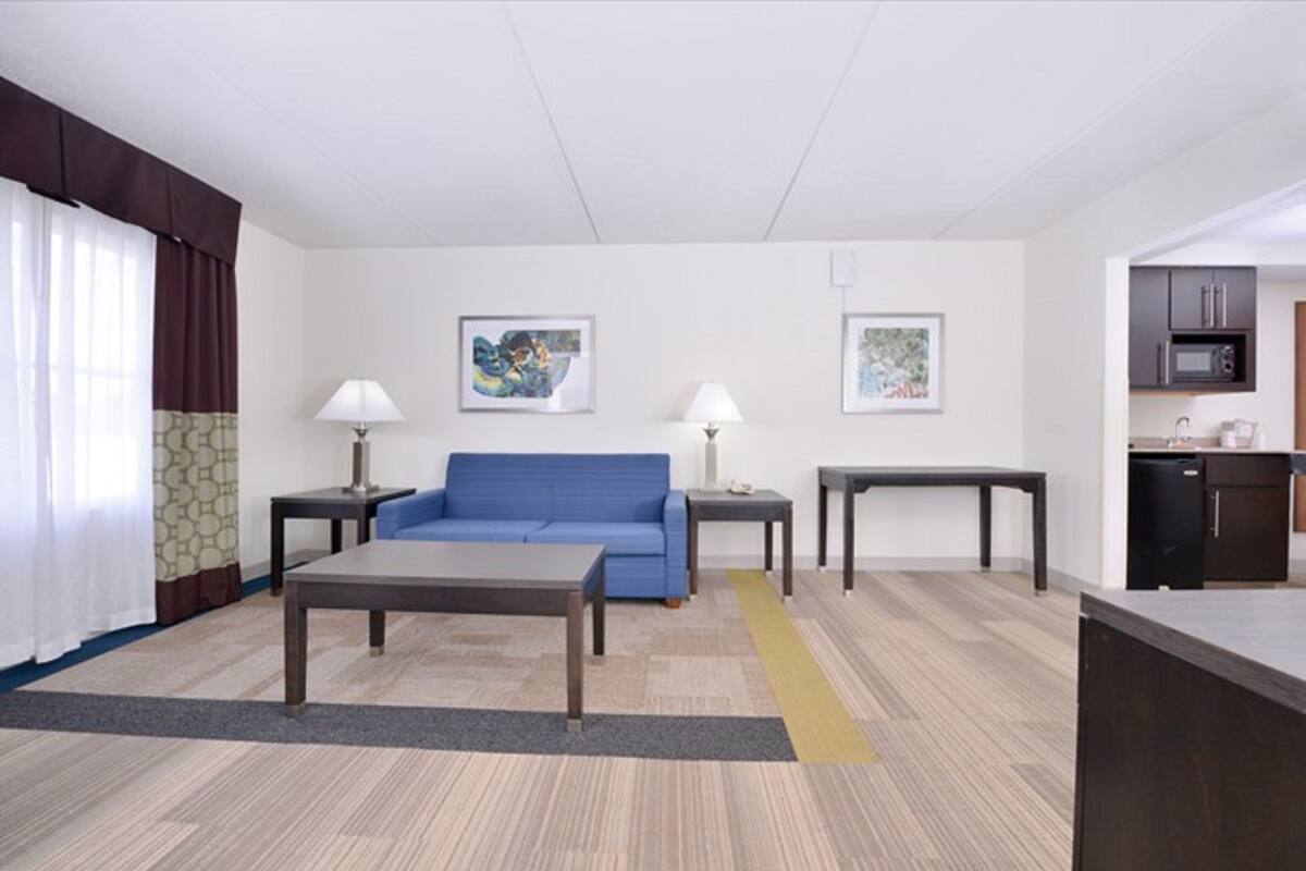 Una habitación de hotel moderna con un sofá azul, dos mesas, una mesa de centro y una cocina con microondas y armarios.