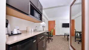 Una habitación de hotel compacta con kitchenette, zona de comedor y televisor montado en la pared.