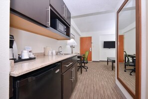 Una habitación de hotel compacta con kitchenette, zona de comedor y televisor montado en la pared.